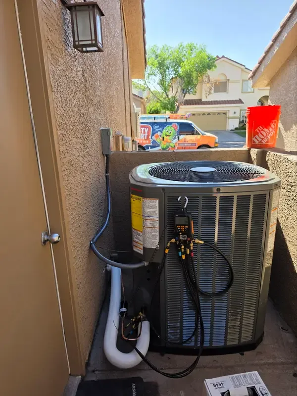 A Frosty Desert Heating & Air service call — AC condenser being serviced with gauges, company van in the background